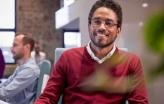 Young man sitting at desk in office, smiling at the camera