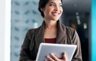 A woman holds a tablet and stares out the window with a smile.