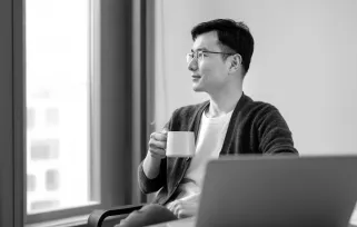 man drinking coffee at laptop looking out window