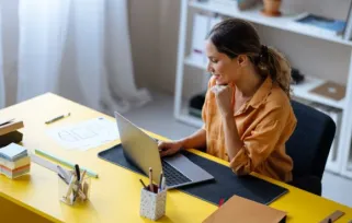 woman wearing yellow working on laptop at desk