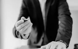 man with head out of shot, presenting a pen across a table