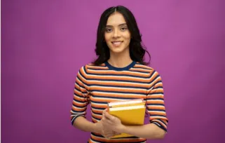 student intern holding books standing against a purple background