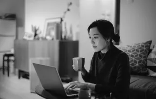 woman working on a laptop while sitting on the couch with a cup of coffee