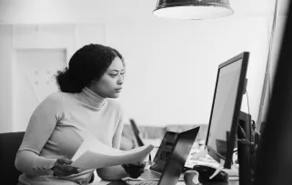 Woman Holding%20papers Looking%20at%20computer Sitting%20at%20deskB%26W Png