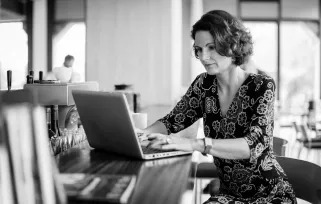 A woman sits at her desk in the office and she's typing on her laptop.