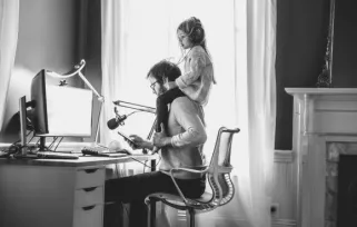 dad working at computer with young daughter sitting on his shoulders