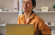 Cheerful female professional in a bright office smiling joyfully while working on her laptop