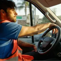 A young delivery person driving his van during a shift at sunset