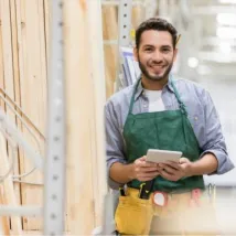 man working in lumber yard holding a digital tablet while smiling at the camera