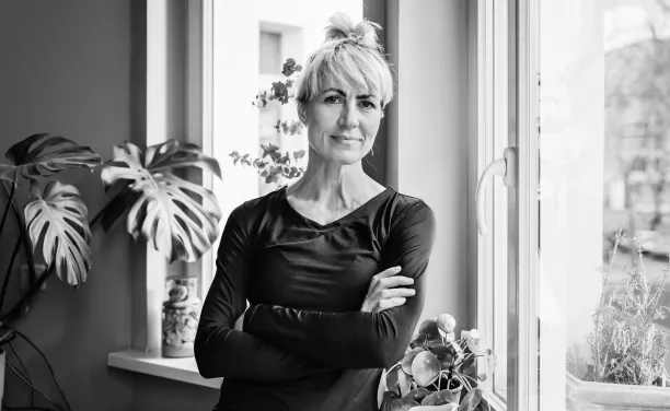 Frau verschränkt die Arme und lehnt an Fenster.